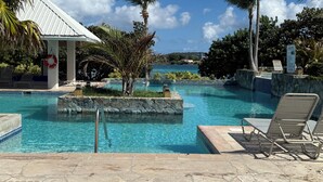 Une piscine d’un bleu éclatant, avec des chaises longues, des palmiers et un bâtiment blanc orné d’une bouée de sauvetage.