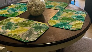 Un coin repas avec une table ronde, des sets de table à motifs tropicaux et un bol décoratif.