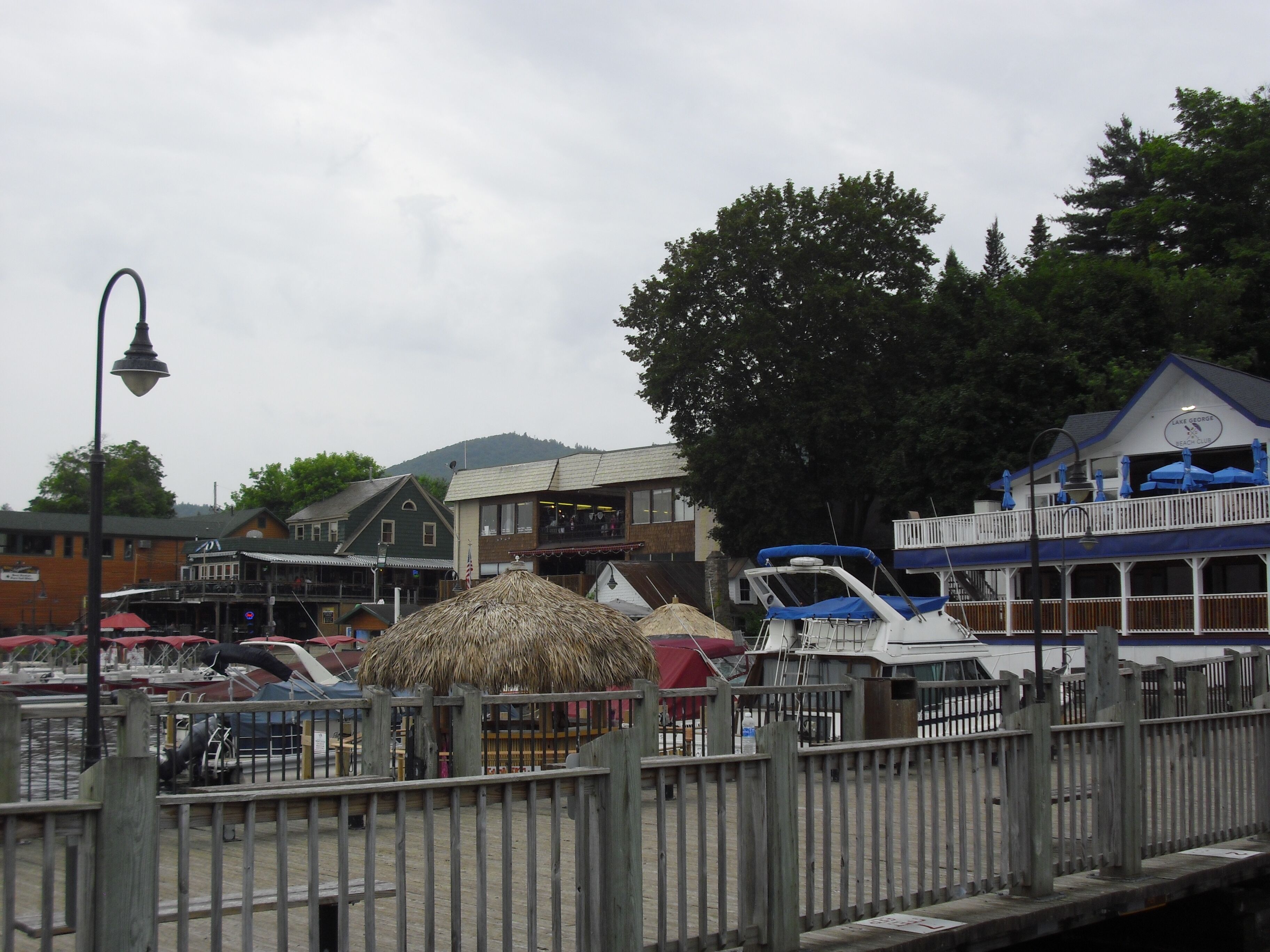 A waterfront area with a wooden dock, a thatched-roof structure, and a building labeled "Lake George Beach Club."