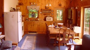Interno di una baita in legno con zona pranzo, angolo cottura e un'ampia finestra.