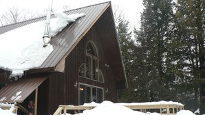 Una baita in legno con tetto spiovente, ampie finestre e un patio in legno di fronte.