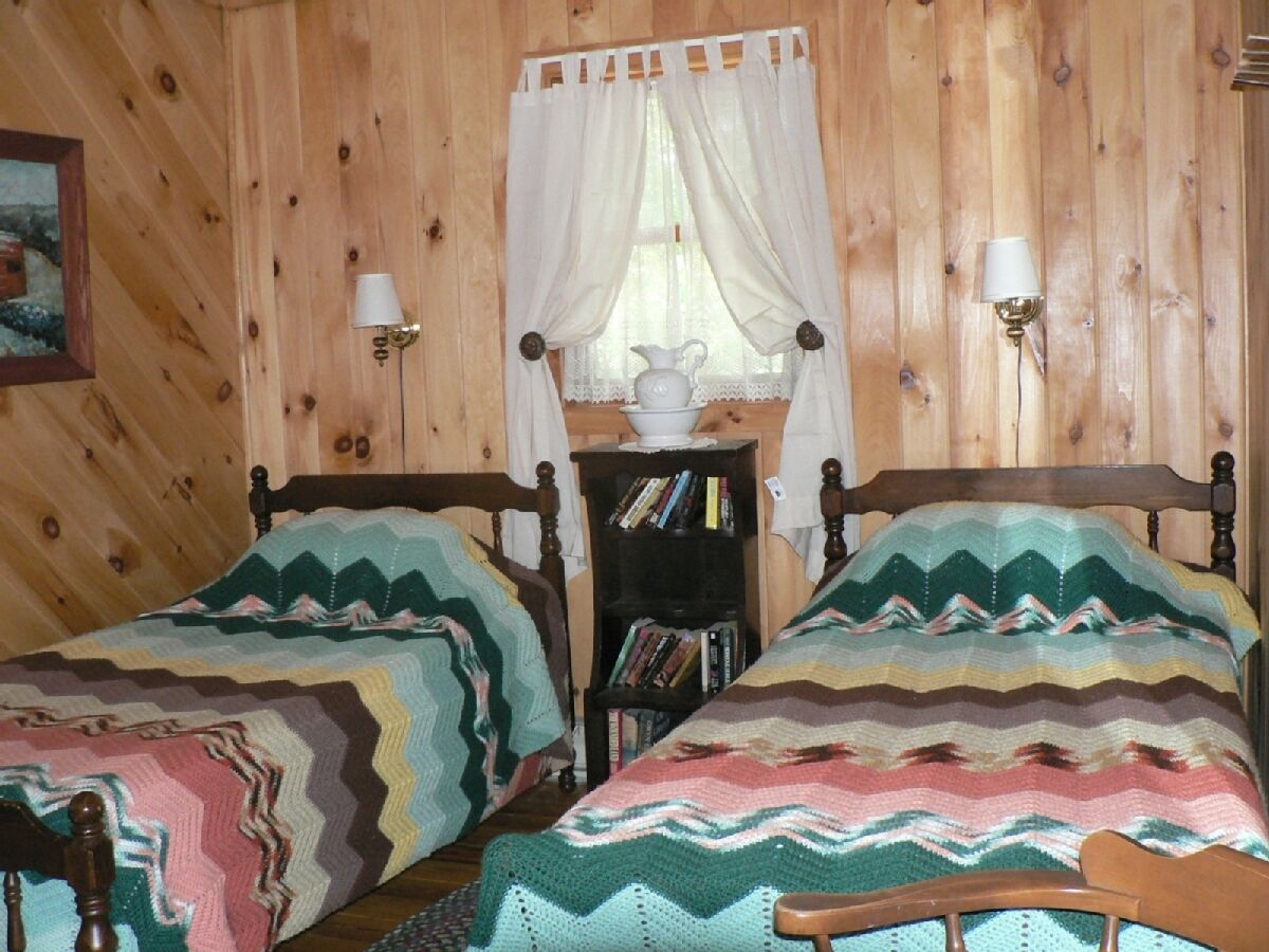 Une pièce en bois avec deux lits, une table de chevet avec des livres, une lampe et une fenêtre avec des rideaux.