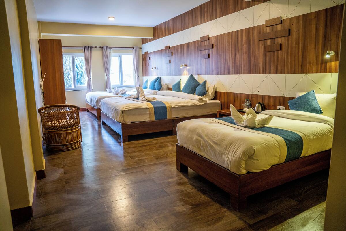 A hotel room with two beds, a wooden floor, a wicker chair, and a view of the outdoors.