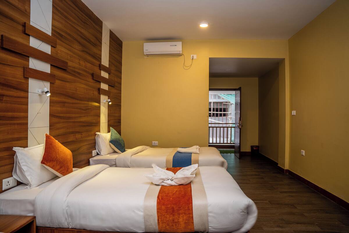 A hotel room with two beds, wooden paneling on the walls, an air conditioning unit, and a view of the outside balcony.