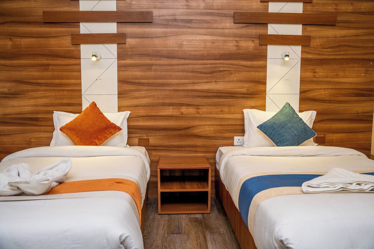 A hotel room with two beds, wooden headboard, white bedding, and a small wooden nightstand between the beds.
