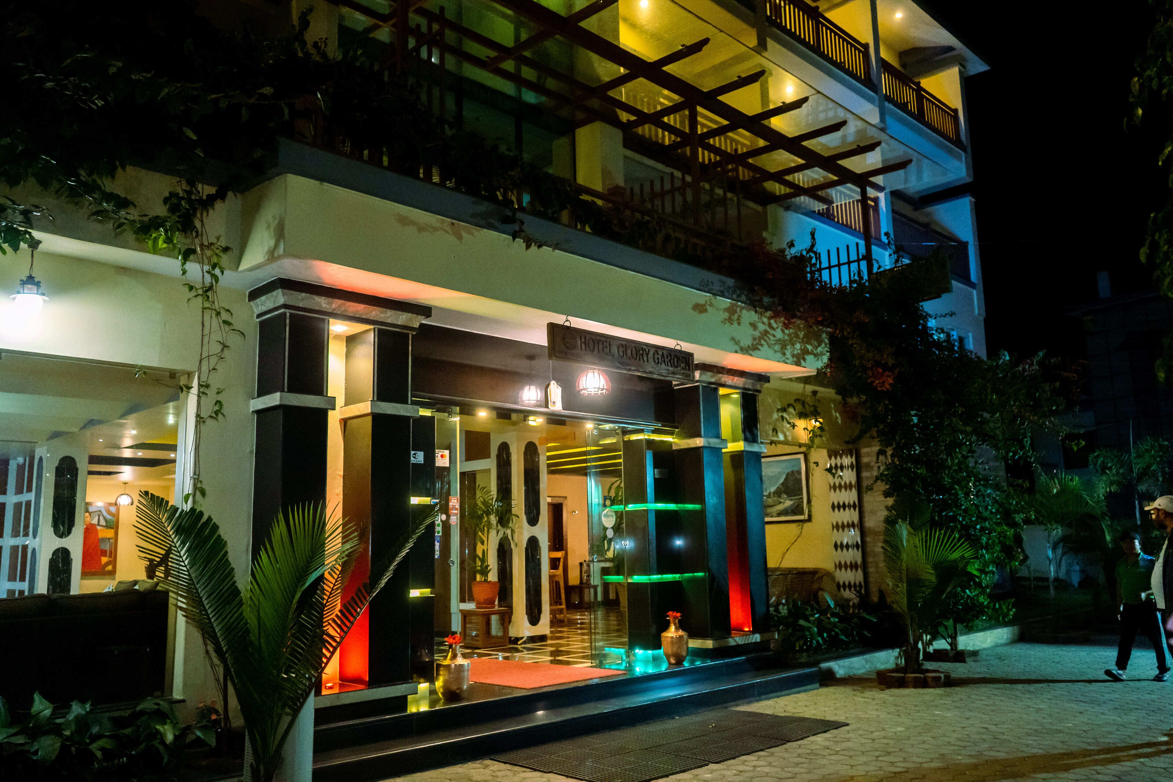 A hotel entrance with a glass facade, a sign reading "Hotel Glory Garden," and a balcony with railings.