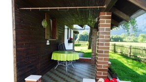 A covered outdoor seating area with a table and chairs, a brick wall, and a garden view. - Ferienwohnung für 4 Personen (75 qm) (Kiefersfelden)