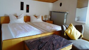 A bedroom with two beds, a wooden ceiling, a radiator, a mirror, and a window with a view. - Ferienwohnung für 4 Personen (75 qm) (Kiefersfelden)