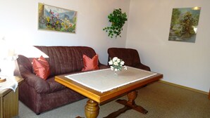 A living room with a brown leather sofa, a wooden coffee table, and two paintings on the walls. - Ferienwohnung für 4 Personen (75 qm) (Kiefersfelden)