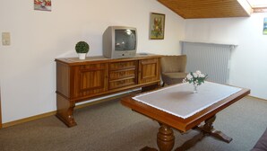 A room with a wooden ceiling, a television on a cabinet, a table with a vase, and a radiator. - Ferienwohnung für 4 Personen (75 qm) (Kiefersfelden)