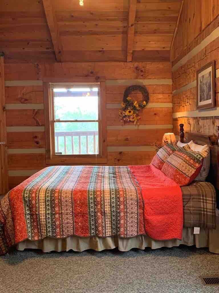 A log cabin bedroom with a bed, a window, a wall wreath, and a framed picture.