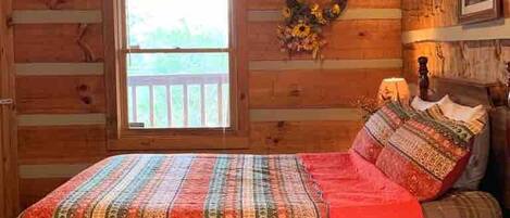 A log cabin bedroom with a bed, a window, a wall wreath, and a framed picture.