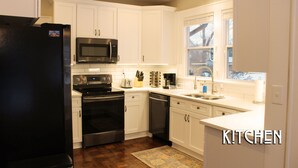 Una cocina con armarios blancos, un refrigerador negro, electrodomésticos de acero inoxidable y una ventana con vistas.
