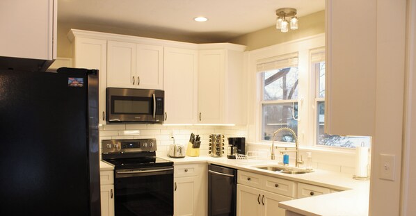 A kitchen with white cabinets, a black refrigerator, stainless steel appliances, and a window with a view.