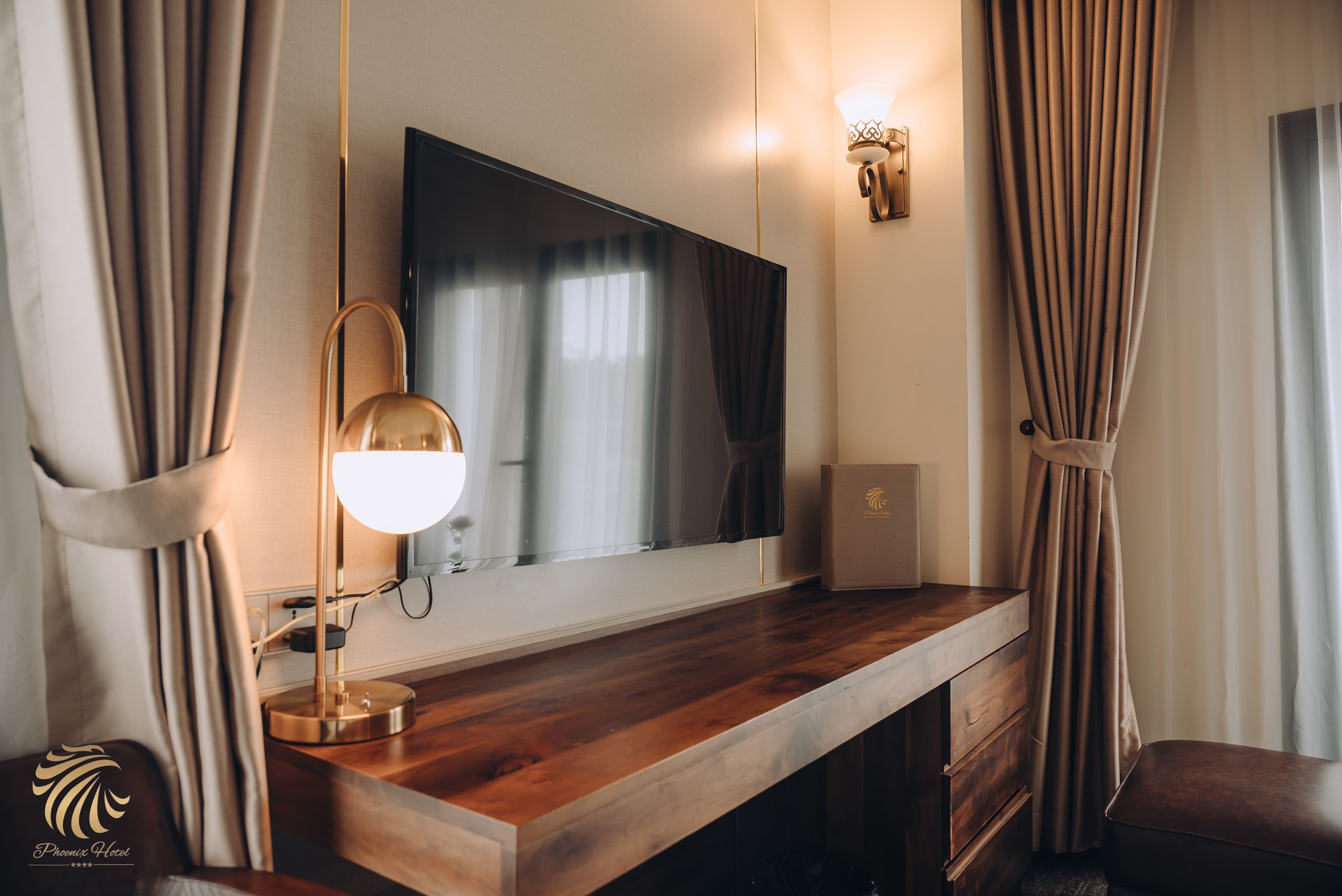 Una habitación de hotel con un escritorio de madera, un espejo grande, una lámpara de pared y cortinas.