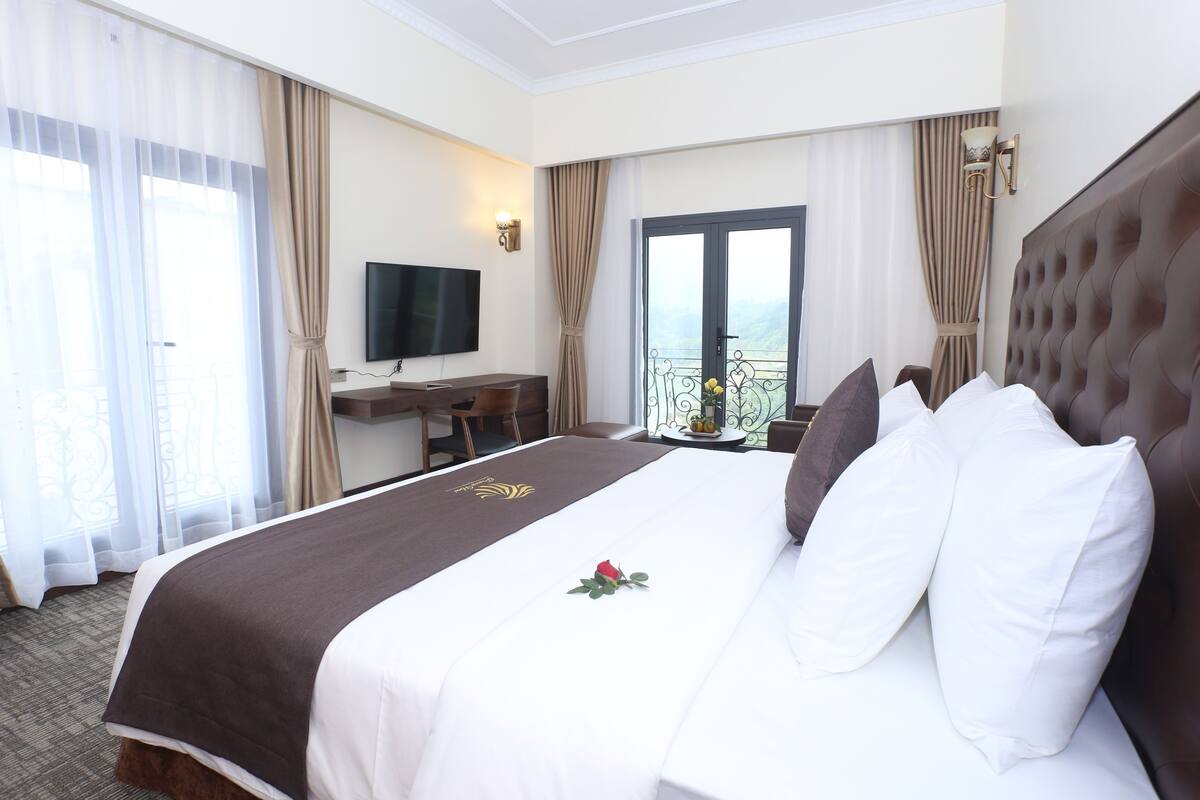 Une chambre d’hôtel avec un grand lit, une télévision à écran plat, un bureau et un balcon avec vue.