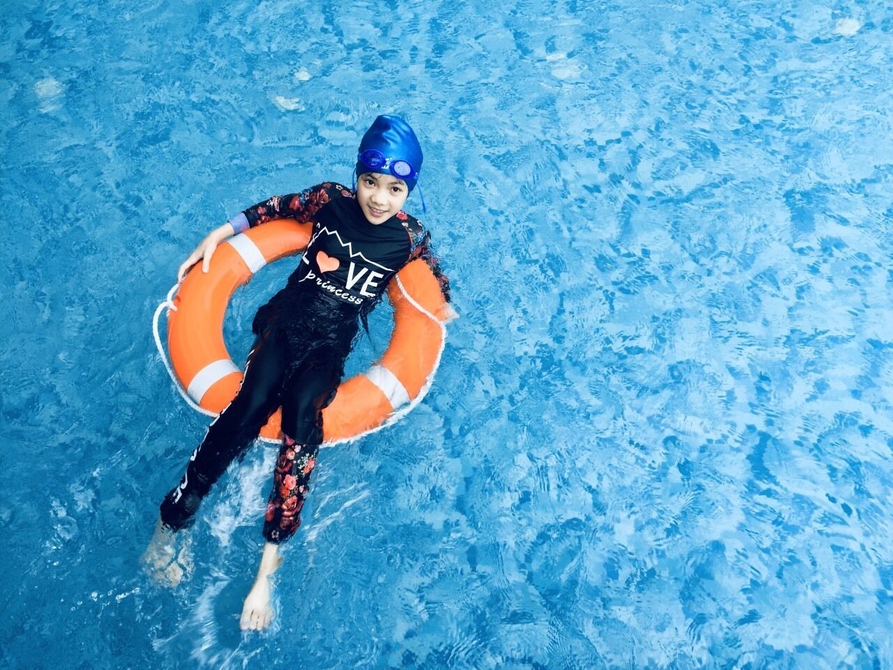 Une personne flotte dans une piscine, tenant un bouée de sauvetage orange.