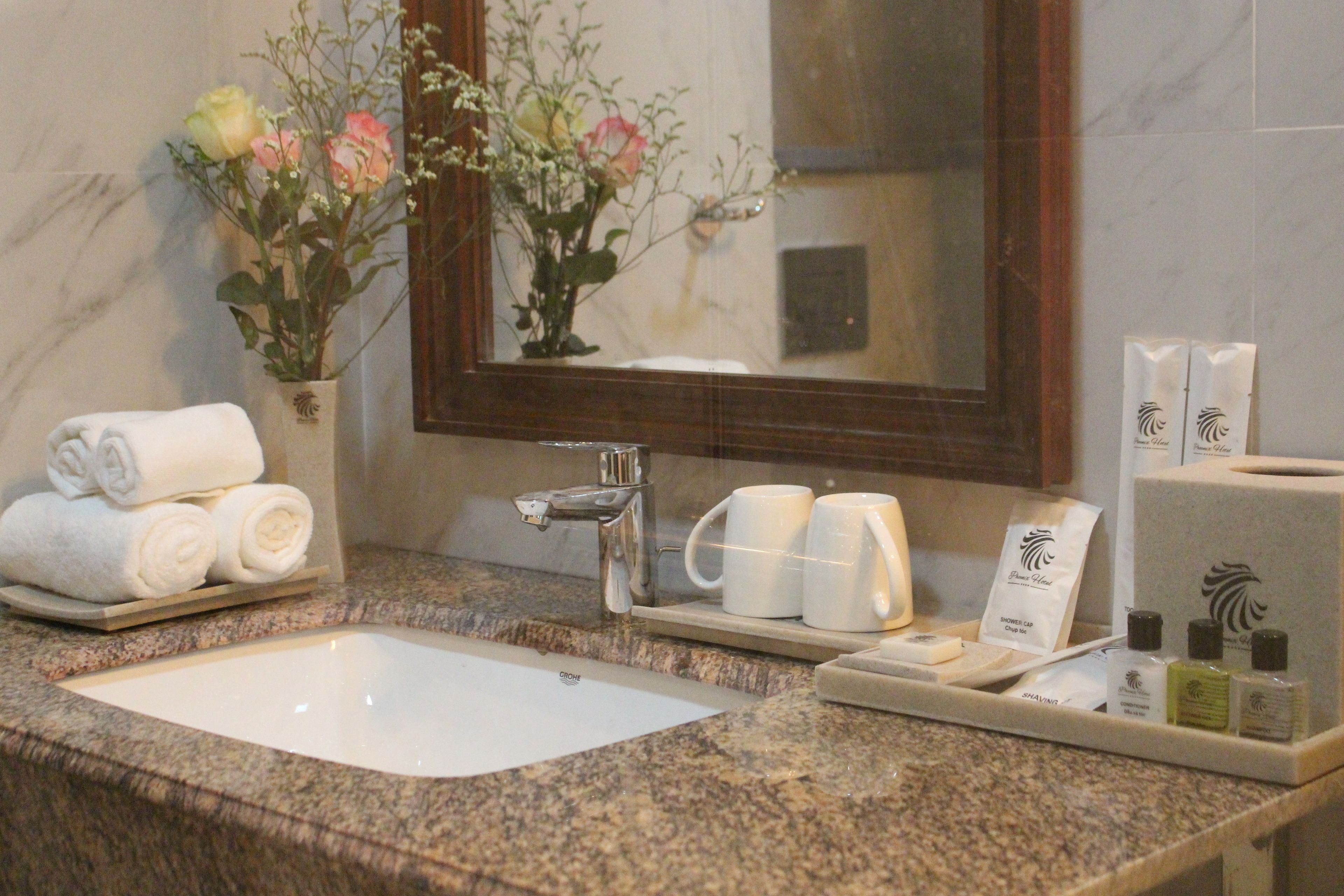 Uma casa de banho com lavatório de mármore, espelho, porta-toalhas com toalhas dobradas, bandeja com artigos de higiene e um vaso com flores.