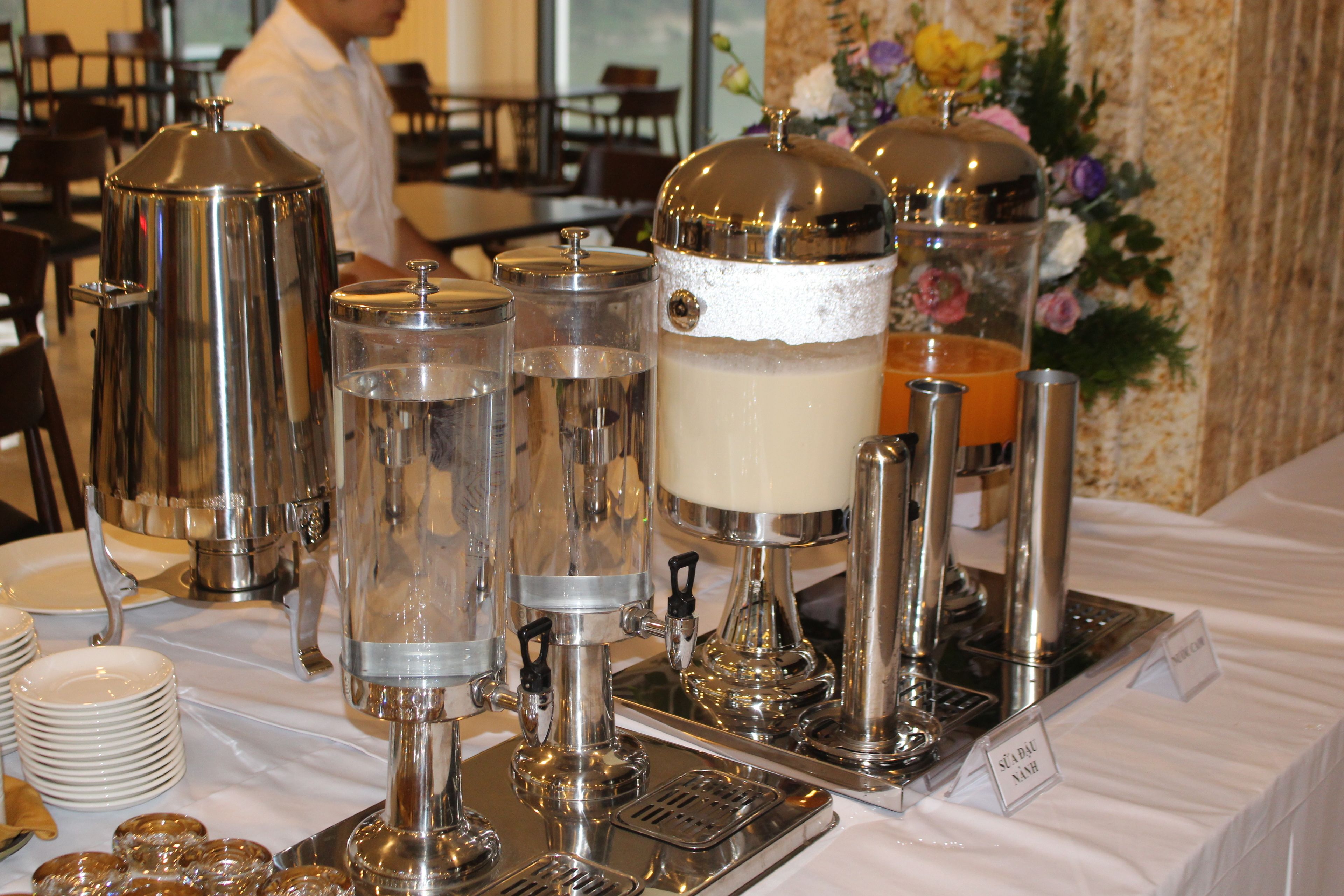 A buffet setup with various food dispensers and a floral arrangement in the background.