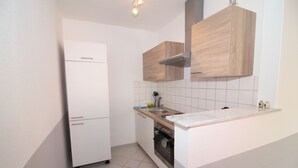 Una cocina compacta con un refrigerador blanco, gabinetes de madera, una campana extractora de acero inoxidable y salpicadero de azulejos.