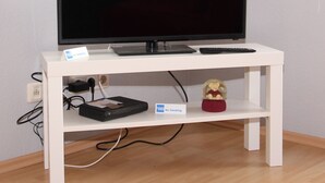 Un mueble blanco para televisor con un televisor de pantalla plana, una regleta de enchufes y un cartel de 'No Smoking'.
