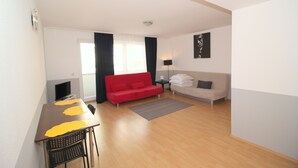 Una sala moderna con un sofá rojo, un sofá beige, una mesa de comedor con individuales amarillos y un televisor sobre un mueble.