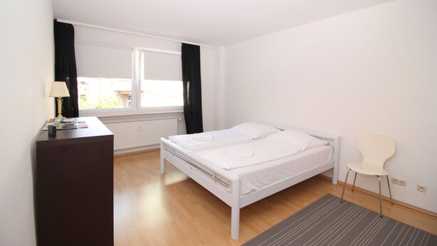 Un dormitorio con cama, escritorio, silla y ventana con cortinas.