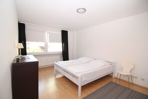 A bedroom with a bed, a desk, a chair, and a window with curtains. - Kaiser Apartments (Offenbach am Main)