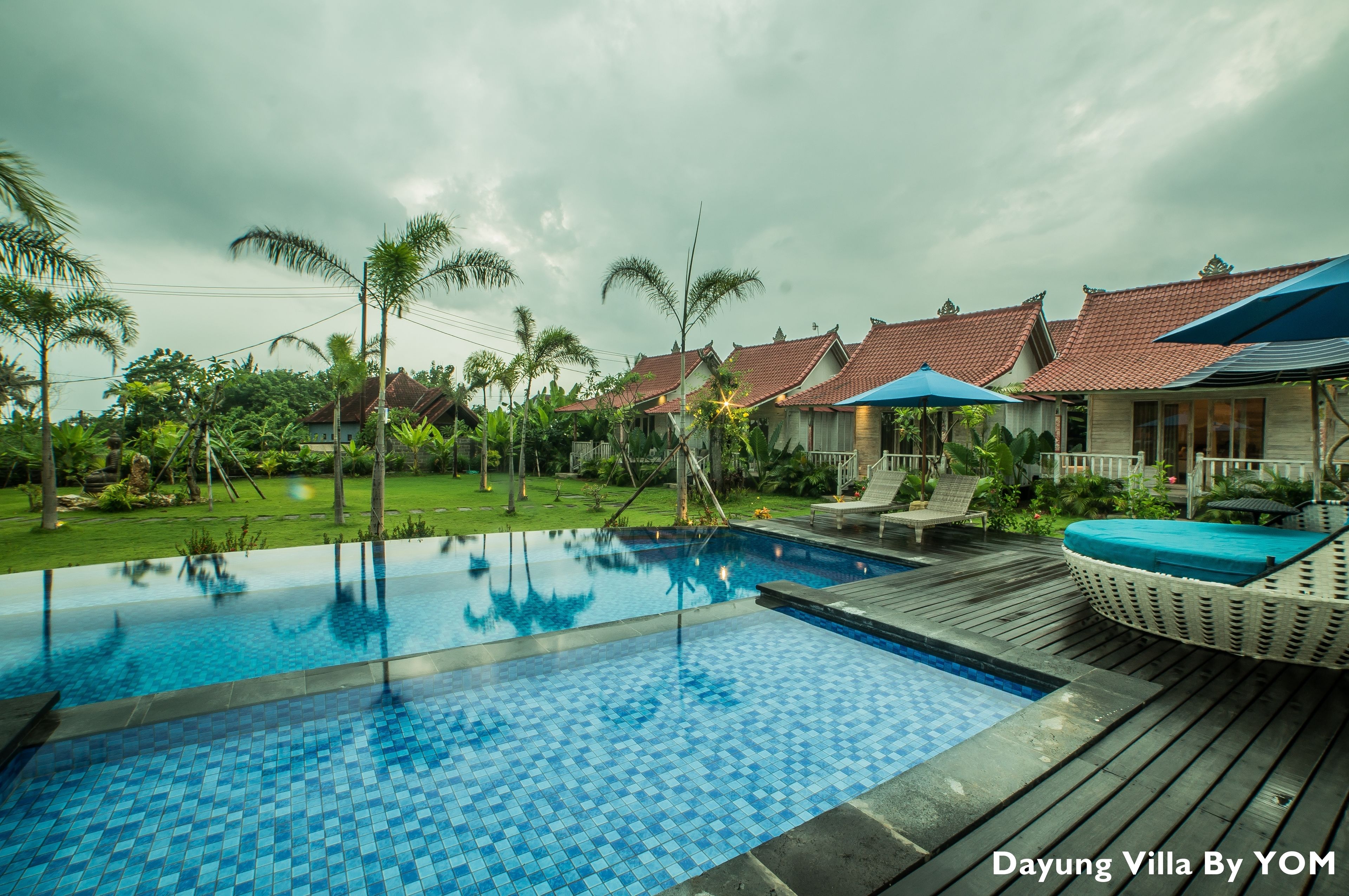 A swimming pool with a tiled deck, surrounded by palm trees and a wooden deck.