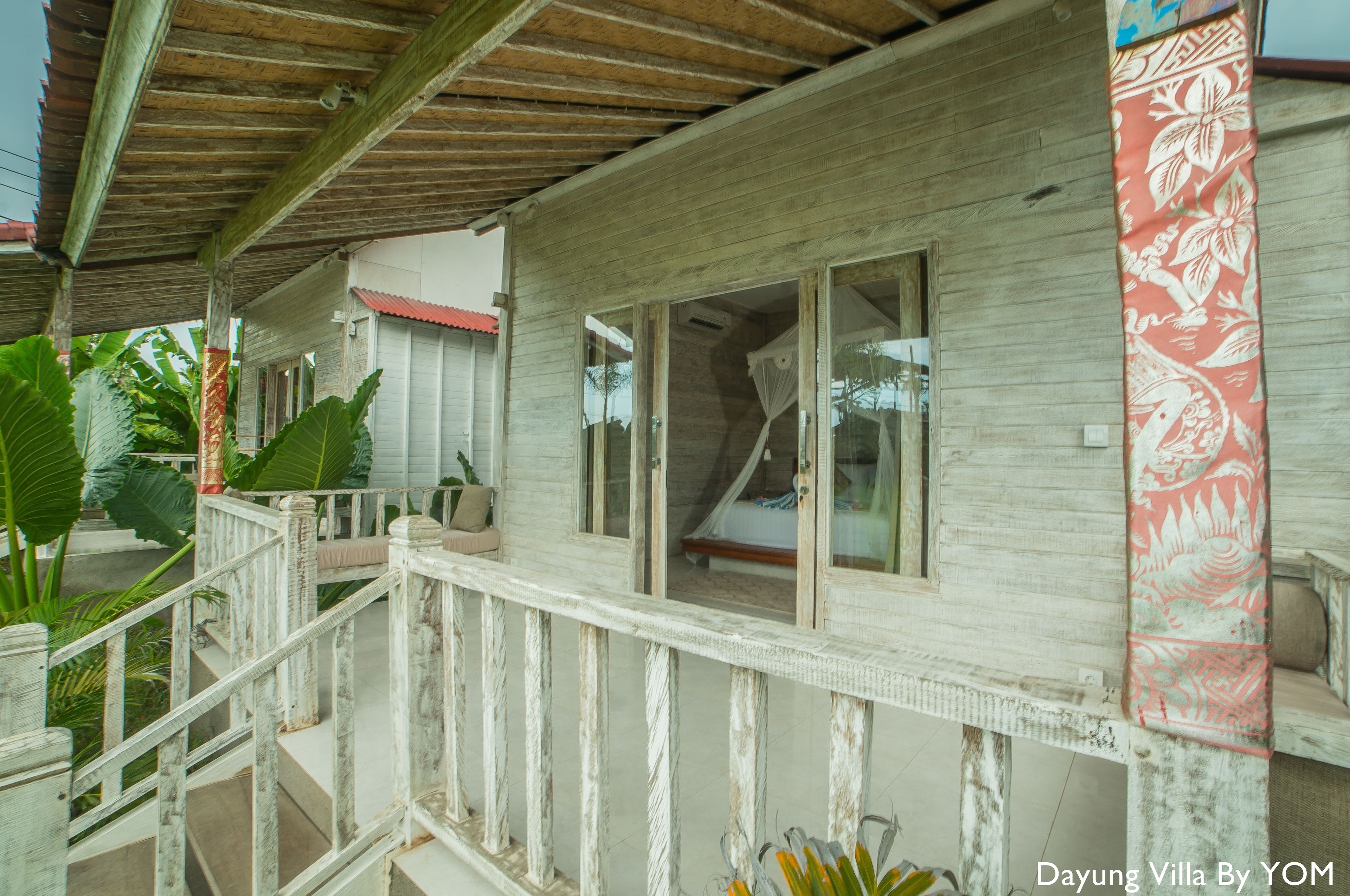 Une villa en bois dotée d’un balcon, de grandes fenêtres et d’un rideau rouge à motifs.
