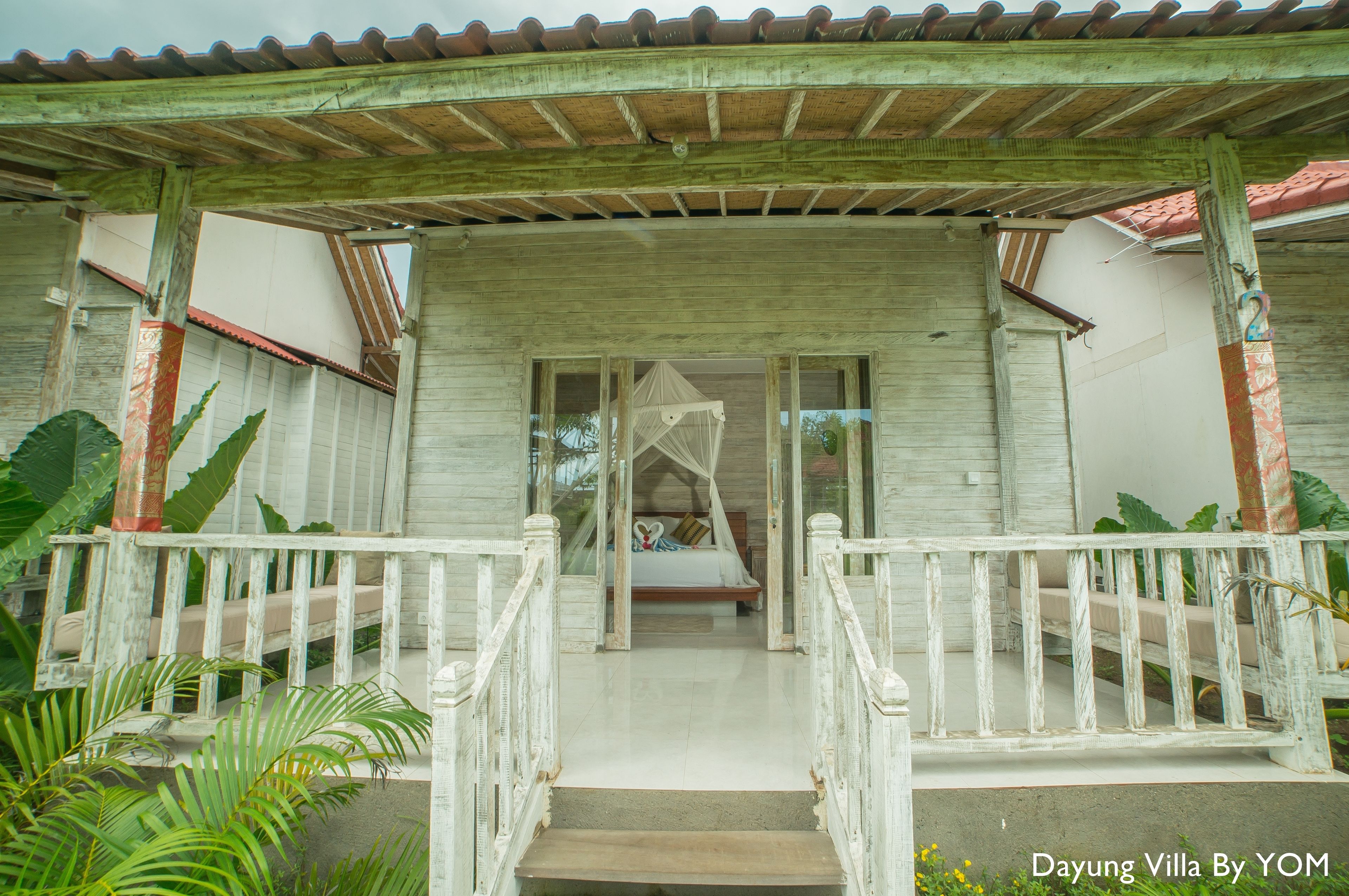 A wooden villa with a covered porch, a bed with a canopy, and a staircase leading to the entrance.