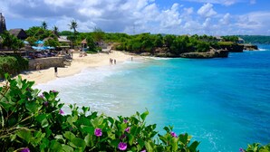 Een strand met helder turquoise water, een zandstrand en weelderige begroeiing.