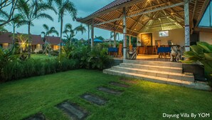 Een villa met een overdekte patio, treden die naar de ingang leiden en een Boeddha-beeld.