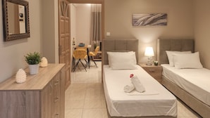 A hotel room with two beds, a dining area with a table and chairs, a mirror, and a painting on the wall. - Chrissomallis Apartments (Skiathos)