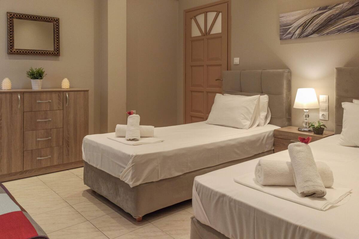 A hotel room with two beds, a wooden wardrobe, a mirror, a door, and a wall with a painting.