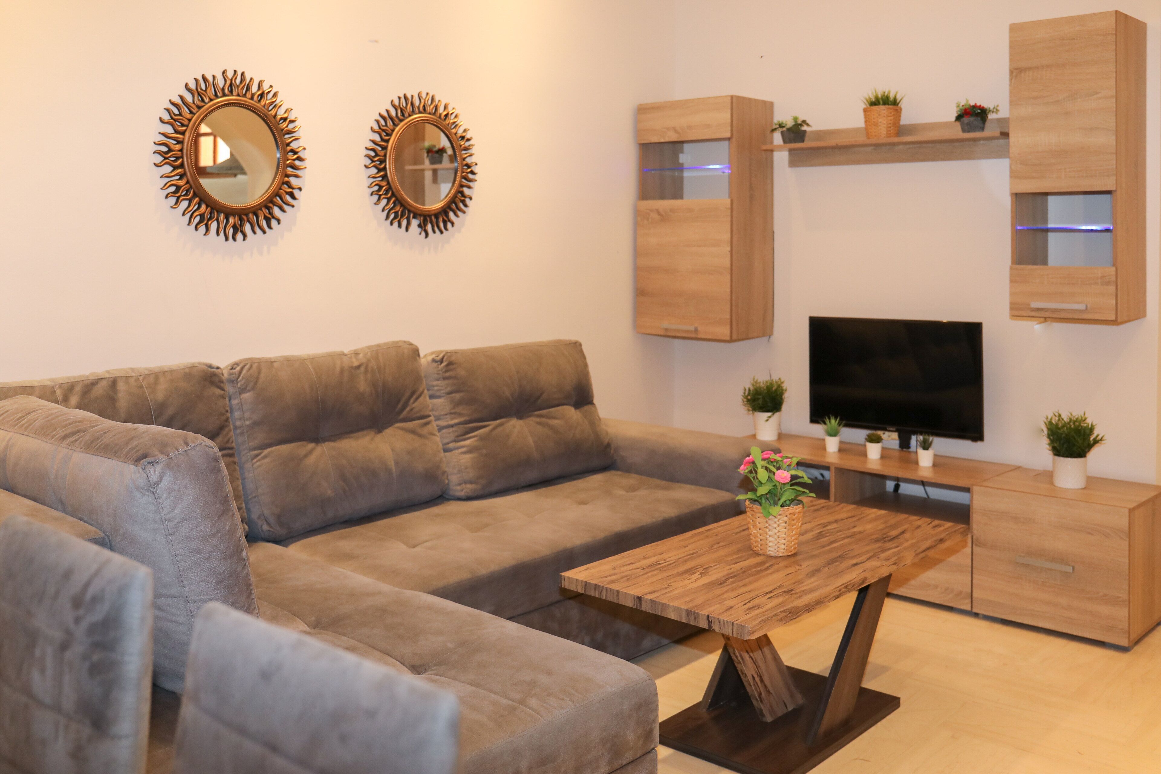 Un salon moderne avec un canapé d’angle, une table basse en bois, un téléviseur à écran plat et des meubles de rangement en bois intégrés.
