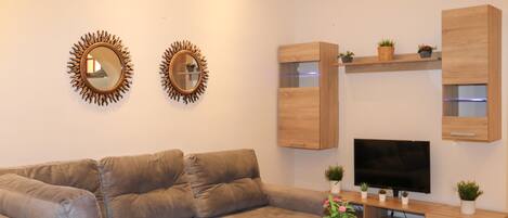 Un salon moderne avec un canapé d’angle, une table basse en bois, un téléviseur à écran plat et des meubles de rangement en bois intégrés.