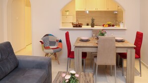A modern living room with a grey sofa, a dining table with red chairs, and a kitchen visible through an arched window. - Chrissomallis Apartments (Skiathos)