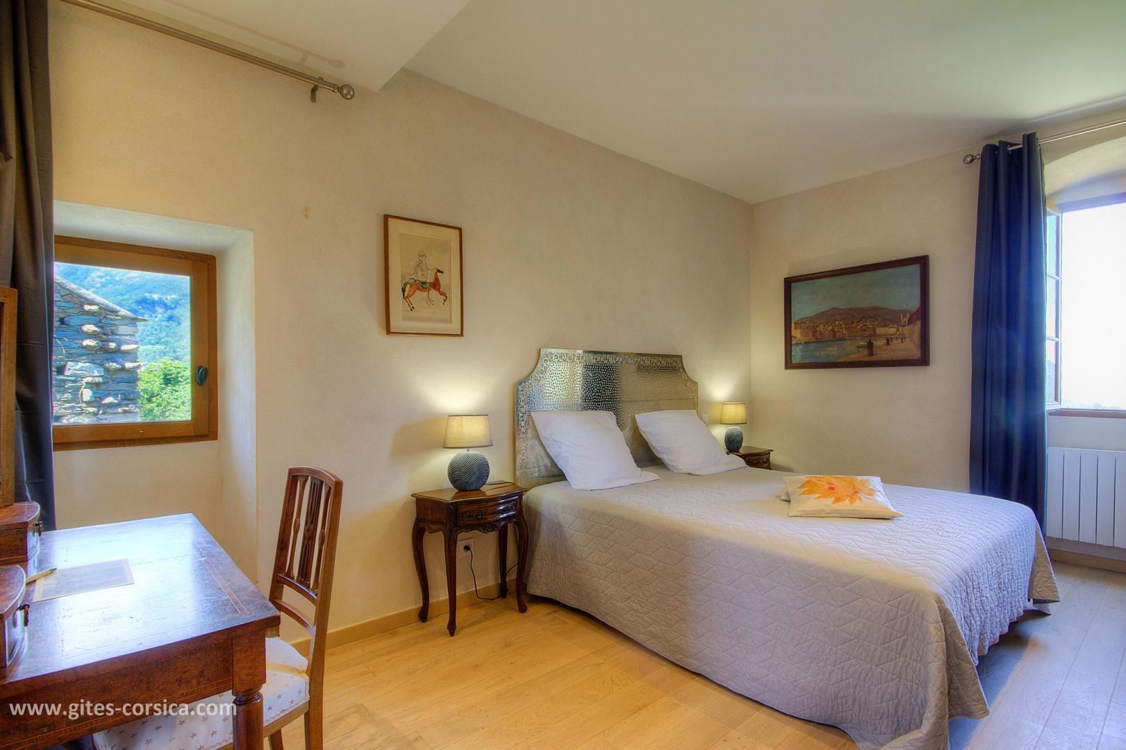 Slaapkamer met een bed, nachtkastje, lamp, stoel en uitzicht op een berg door een raam.