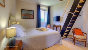 A bedroom with a bed, a nightstand, a lamp, a chair, a painting, a TV, and a ladder. - Castellu d'Orezza (Carcheto-Brustico)