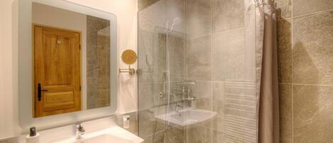 Un bagno moderno con una porta in legno, uno specchio grande, una cabina doccia in vetro e un lavandino bianco.
