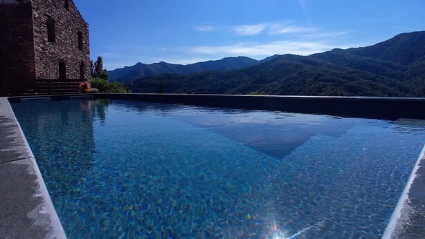 A clear blue pool with a stone structure on one side and a mountainous landscape in the background. - Castellu d'Orezza (Carcheto-Brustico)