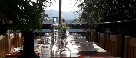 Un área de comedor al aire libre con una mesa larga dispuesta para dos personas, rodeada de sillas, bajo un toldo.