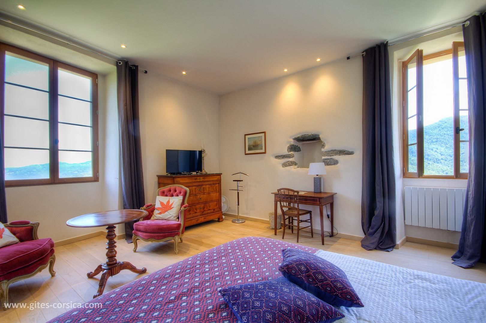 Ein Hotelzimmer mit Bett, Schreibtisch, Stuhl, Kommode und Fernseher.
