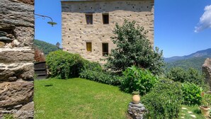 A stone building with a flat roof, surrounded by a well-maintained garden and a clear blue sky. - Castellu d'Orezza (Carcheto-Brustico)