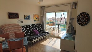 A living room with a sofa, a dining table, a ceiling fan, and a dartboard. - CALAFELL 5 BEACH WITH: POOL, BEACH, PARKING, SUPERMARKETS / MAC-DONALS (Calafell)