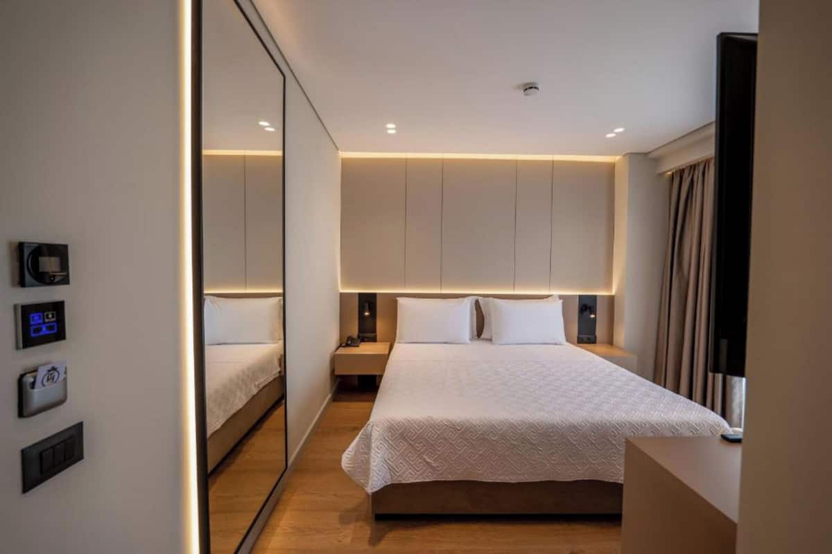 A modern hotel room with a large bed, bedside controls, and a mirror.