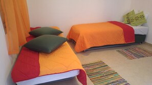 Two single beds with orange and red bedding, green pillows, and a colorful woven rug on the floor. - Elifaz Kibbutz Desert Hospitality (Hevel Eilot)
