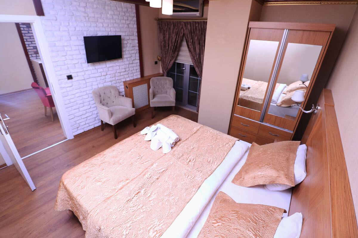 A bedroom with a bed, a chair, a wardrobe, a television on the wall, and a window with curtains.