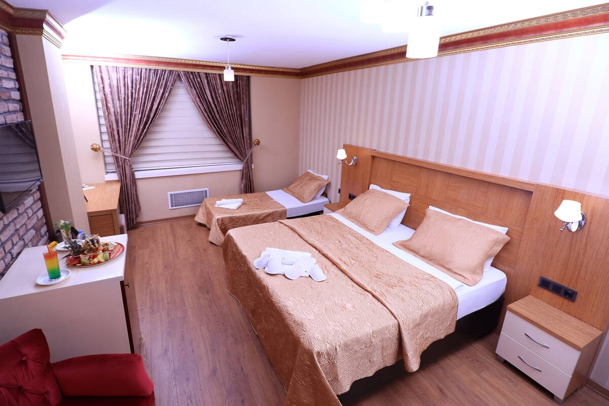 A hotel room with two beds, a small desk with a fruit platter, a red chair, and a wooden floor.